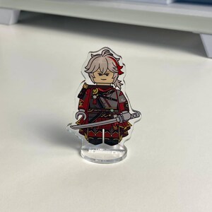 K&ouml;nnte beinhalten: Eine transparente Acrylfigur eines Charakters mit wei&szlig;en Haaren und roten Akzenten, gekleidet in einem rot-grauen Outfit, der ein Schwert h&auml;lt. Die Figur ist im Blockstil gestaltet und steht auf einem transparenten Sockel.