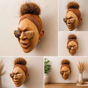 Könnte beinhalten: Eine Holzskulptur eines Frauengesichts mit Sonnenbrille. Die Skulptur hat eine Dutt-Frisur und kleine Ohrringe. Die Sonnenbrille ist aus einer anderen Holzart gefertigt. Die Skulptur ist an einer hellen Wand befestigt.