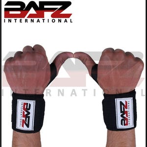 May include: A pair of black wrist wraps featuring a white rectangular patch with the red and black BAFZ INTERNATIONAL logo. The wraps include a black thumb loop and are secured around the wrists, displaying the brand name clearly on each side.
