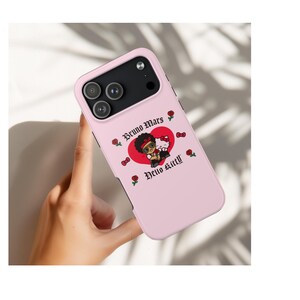 Puede incluir: Funda de tel&eacute;fono rosa claro con una ilustraci&oacute;n de dibujos animados de Bruno Mars y Hello Kitty dentro de un coraz&oacute;n rojo. La funda tiene las palabras "Bruno Mars" y "Hello Kitty" en una fuente decorativa, con rosas y lazos.