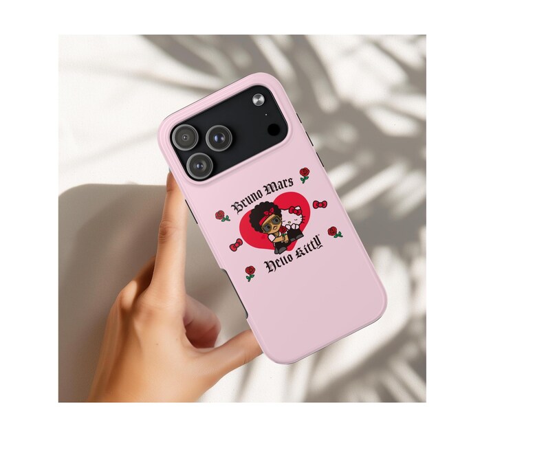 Puede incluir: Funda de tel&eacute;fono rosa claro con una ilustraci&oacute;n de dibujos animados de Bruno Mars y Hello Kitty dentro de un coraz&oacute;n rojo. La funda tiene las palabras "Bruno Mars" y "Hello Kitty" en una fuente decorativa, con rosas y lazos.