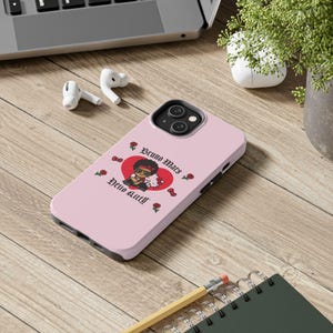 Puede incluir: Funda de tel&eacute;fono rosa con un gr&aacute;fico de Bruno Mars y Hello Kitty dentro de un coraz&oacute;n rojo. La funda tiene un borde negro y est&aacute; decorada con gr&aacute;ficos de rosas y corazones. La funda del tel&eacute;fono est&aacute; sobre una superficie de madera con un port&aacute;til, auriculares y una planta.