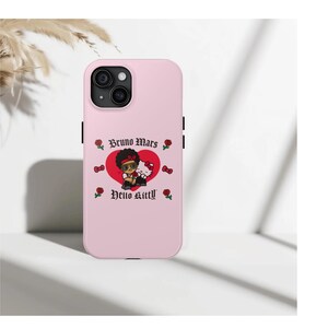Puede incluir: Funda de iPhone rosa claro con un gr&aacute;fico de Bruno Mars y Hello Kitty en un coraz&oacute;n rojo. La funda tiene botones laterales negros y el texto "Bruno Mars" y "Hello Kitty". Tambi&eacute;n se presentan rosas y lazos rojos.
