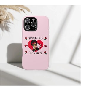 Puede incluir: Funda de tel&eacute;fono rosa claro con un gr&aacute;fico de Bruno Mars y Hello Kitty. El dise&ntilde;o incluye un coraz&oacute;n rojo, rosas y el texto "Bruno Mars" y "Hello Kitty". La funda tiene un m&oacute;dulo de c&aacute;mara negro.