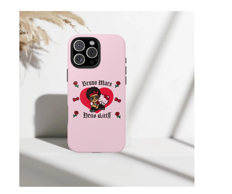 Puede incluir: Funda de tel&eacute;fono rosa claro con un gr&aacute;fico de Bruno Mars y Hello Kitty. El dise&ntilde;o incluye un coraz&oacute;n rojo, rosas y el texto "Bruno Mars" y "Hello Kitty". La funda tiene un m&oacute;dulo de c&aacute;mara negro.