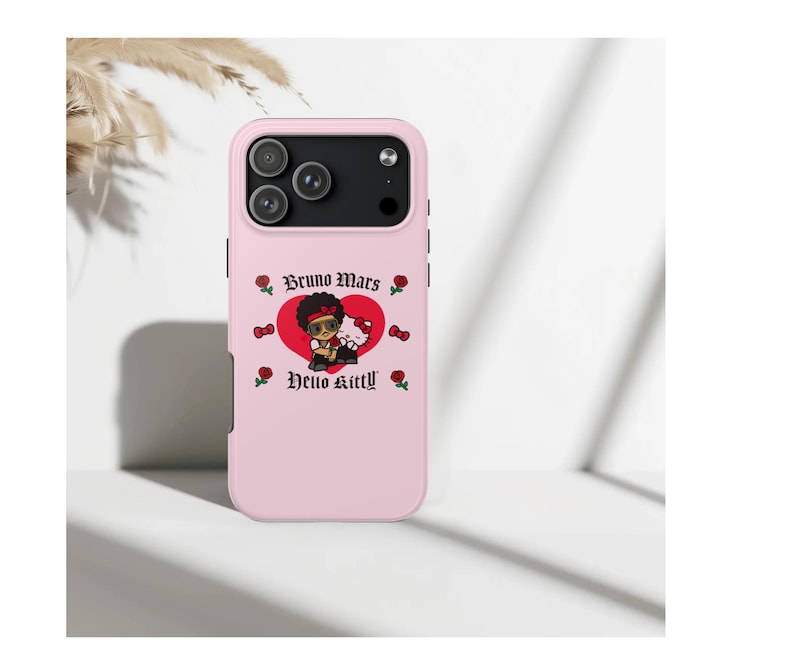 Puede incluir: Funda de tel&eacute;fono rosa con un gr&aacute;fico de dibujos animados de un personaje con gafas de sol, sobre un coraz&oacute;n rojo. El texto "Bruno Mars" y "Hello Kitty" tambi&eacute;n est&aacute; presente, junto con motivos de rosas y corazones.