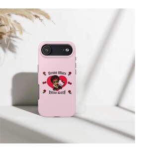 Puede incluir: Funda de tel&eacute;fono rosa con un gr&aacute;fico de dibujos animados de Bruno Mars y Hello Kitty. El dise&ntilde;o incluye un coraz&oacute;n rojo, rosas y el texto "Bruno Mars" y "Hello Kitty" en fuente g&oacute;tica. La funda tiene un recorte para la c&aacute;mara.