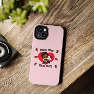 Puede incluir: Funda de tel&eacute;fono rosa con un gr&aacute;fico de Bruno Mars y Hello Kitty dentro de un coraz&oacute;n rojo. La funda tiene el texto "Bruno Mars" y "Hello Kitty" en una fuente decorativa, con rosas y lazos.