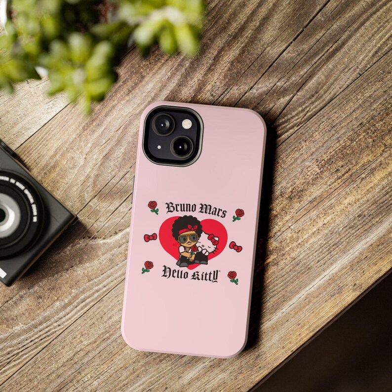 Puede incluir: Funda de tel&eacute;fono rosa con un gr&aacute;fico de Bruno Mars y Hello Kitty dentro de un coraz&oacute;n rojo. La funda tiene el texto "Bruno Mars" y "Hello Kitty" en una fuente decorativa, con rosas y lazos.