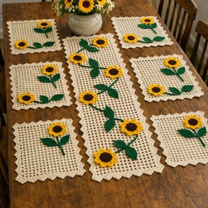 Könnte beinhalten: Ein Holztisch-Set mit einem gehäkelten Sonnenblumen-Tischläufer und passenden Platzsets. Der Läufer und die Platzsets sind cremefarben mit gelben und braunen Sonnenblumen und grünen Blättern. Eine Vase mit Sonnenblumen steht in der Mitte.