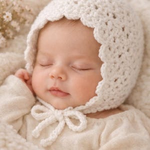 May include: A sleeping baby wearing a white, crocheted bonnet with a scalloped edge and a matching bow. The baby is wrapped in a soft, cream-coloured blanket and wearing a long-sleeved shirt. The overall aesthetic is soft and delicate.