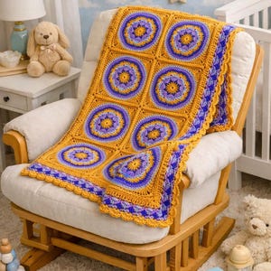 May include: A handmade crochet blanket in shades of gold, purple, and blue, draped over a rocking chair. The blanket features a geometric pattern of circles and squares. The chair is made of wood and has a cream-colored cushion.