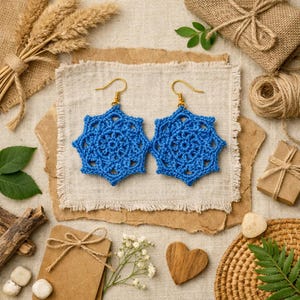 May include: A pair of bright blue crochet earrings featuring a star-shaped design with intricate openwork patterns. Each earring is attached to a gold-toned metal hook, showcasing a detailed, handcrafted textile construction with a vibrant color.