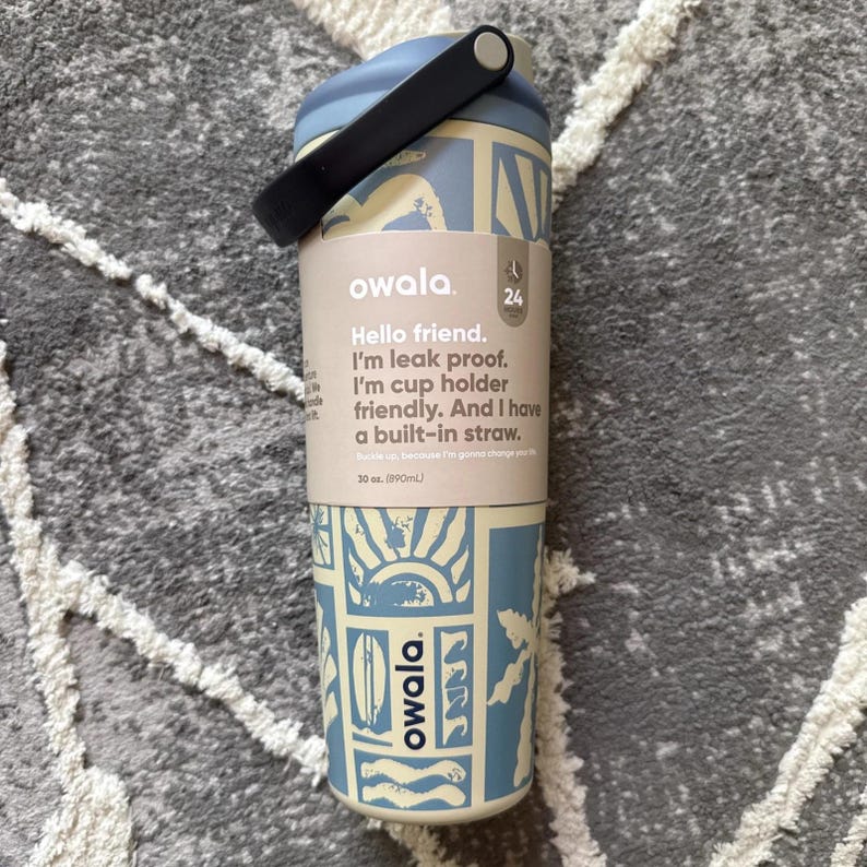 May include: A light blue and cream-colored Owala water bottle with a black handle. The bottle has a patterned design with the text "Hello friend. I'm leak proof. I'm cup holder friendly. And I have a built-in straw." It holds 30 oz.