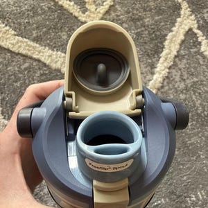 May include: A blue water bottle with a flip-top lid and a FreeSip spout. The bottle has a light blue body with a darker blue cap and a beige lid. The spout is light blue and the lid is open, revealing the interior.