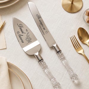 Puede incluir: Un juego de pala para pastel y cuchillo de plata con mangos transparentes facetados estilo cristal. La pala está grabada con los nombres Daniel y Aurora y un diseño de hojas. El cuchillo tiene grabado el texto Por siempre mi y Princesa Hermosa.