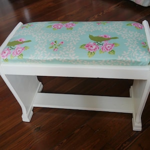 May include: White wooden bench with a floral patterned cushion. The cushion has a light blue background with pink roses and green birds.