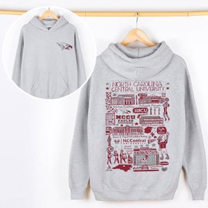 Puede incluir: Una sudadera con capucha gris claro con un bolsillo delantero. El cofre delantero izquierdo tiene un logotipo de &aacute;guila rojo y azul. La parte posterior de la sudadera con capucha presenta un gr&aacute;fico granate con el texto "NORTH CAROLINA CENTRAL UNIVERSITY" y "NCCU EAGLES".