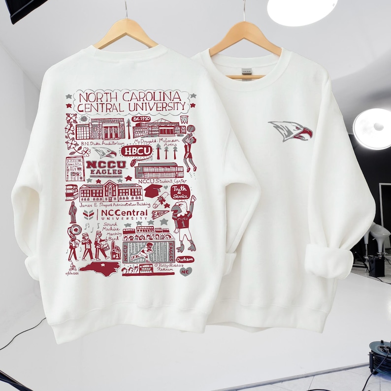 Puede incluir: Sudadera blanca con un gr&aacute;fico granate detallado de los puntos de referencia de la Universidad Central de Carolina del Norte y el texto "NORTH CAROLINA CENTRAL UNIVERSITY". La otra sudadera tiene un logotipo de &aacute;guila granate.