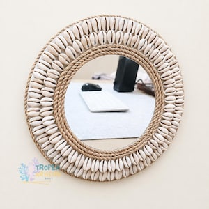 Peut inclure: Miroir rond avec une bordure de coquillages naturels et une bordure en corde. Le miroir reflète un bureau avec un clavier et une souris. Le miroir est un objet décoratif sur le thème côtier ou plage.