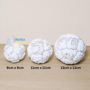 May include: Three spherical decorative objects crafted from white seashells, arranged in increasing size. The spheres are labeled with dimensions of 9cm x 9cm, 11cm x 11cm, and 13cm x 13cm. A logo with the text TROPEA ARTISAN BALI is visible above the smallest sphere.