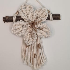 Peut inclure: Une décoration murale en macramé représentant une fleur nouée blanc cassé suspendue à une branche en bois brun foncé. Le centre de la fleur est rehaussé de fil doré métallique, et la frange inférieure comporte de petits enroulements de fil doré.