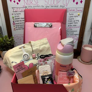 Peut inclure: Une bo&icirc;te cadeau rose contenant un presse-papier rose, un sac fourre-tout en toile cr&egrave;me, une gourde Owala blanche et rose, une montre d'infirmi&egrave;re blanche, un stylo rose, un petit carnet, un tissu &agrave; motifs floraux et diverses petites cartes avec du texte.