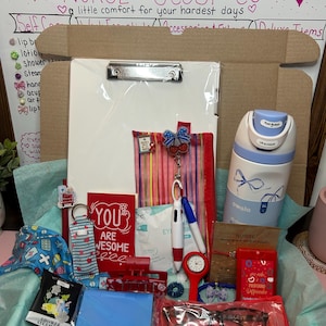 Peut inclure: Un coffret cadeau contenant un presse-papier blanc, une bouteille d'eau Owala bleu clair, une pochette rouge, une carte rouge avec l'inscription YOU ARE AWESOME, une pince &agrave; cheveux rouge, une montre rouge, des lunettes bleues et divers accessoires.