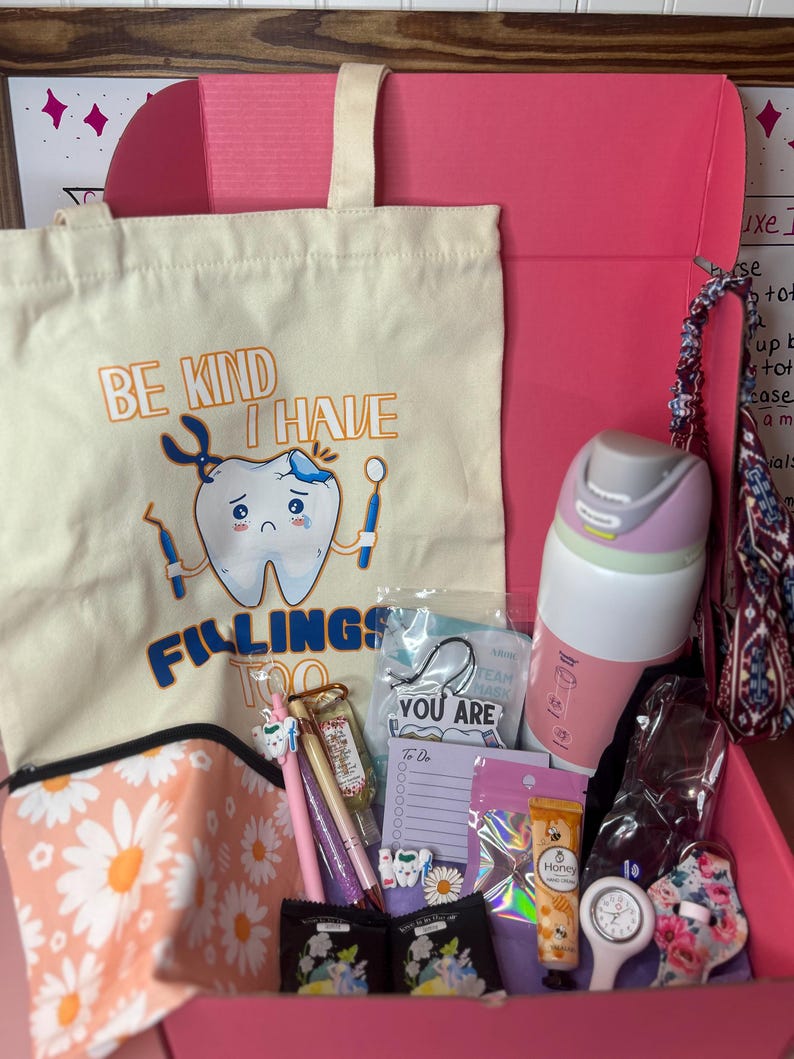 Peut inclure: Une bo&icirc;te cadeau rose contenant un sac fourre-tout cr&egrave;me avec un graphique de dent et le texte BE KIND I HAVE FILLINGS TOO, une gourde rose et blanche, une pochette &agrave; motifs marguerites, des stylos, un bloc-notes, de la cr&egrave;me pour les mains.