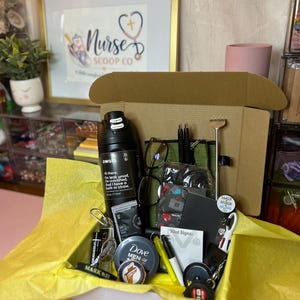 Peut inclure: Une bo&icirc;te cadeau en carton doubl&eacute;e de papier de soie jaune contenant une bouteille d'eau Owala noire de 710 ml, un r&eacute;cipient Dove Men+Care, des lunettes, un carnet noir, un gratte-dos en m&eacute;tal, des stylos, un enrouleur de badge et divers accessoires.