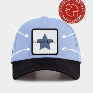 May include: A light blue baseball cap with a black brim and a square patch on the front featuring a blue star and the word america in script. A red circular badge in the top right corner reads INTERCHANGEABLE PATCH SYSTEM with circular arrows.