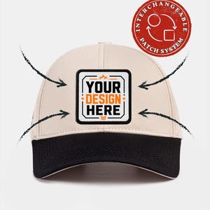 May include: A beige baseball cap with a black brim and a square patch on the front featuring the text YOUR DESIGN HERE in black and orange. Four black arrows point toward the patch. A red circular badge reads INTERCHANGEABLE PATCH SYSTEM.