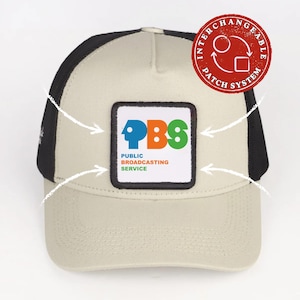 May include: A beige and black trucker hat featuring a square patch with the PBS logo and the text Public Broadcasting Service. A red circular stamp in the upper right corner reads INTERCHANGEABLE PATCH SYSTEM with a circular arrow icon.
