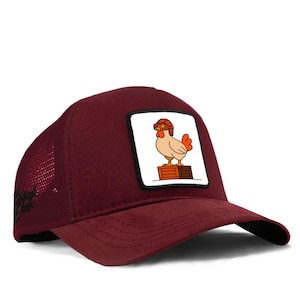 Puede incluir: Gorra de camionero burdeos con parte trasera de malla y visera curva. La parte delantera presenta un parche cuadrado con un dibujo de un pollo con gafas, de pie sobre una caja de madera. Cierre a presión.