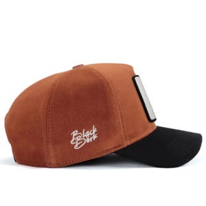 May include: A rust-colored baseball cap with a black brim and a rectangular patch on the side. The side panel features white embroidered text that reads Black B&oslash;rk. The cap has a structured crown and a curved visor, showcasing a two-tone design.