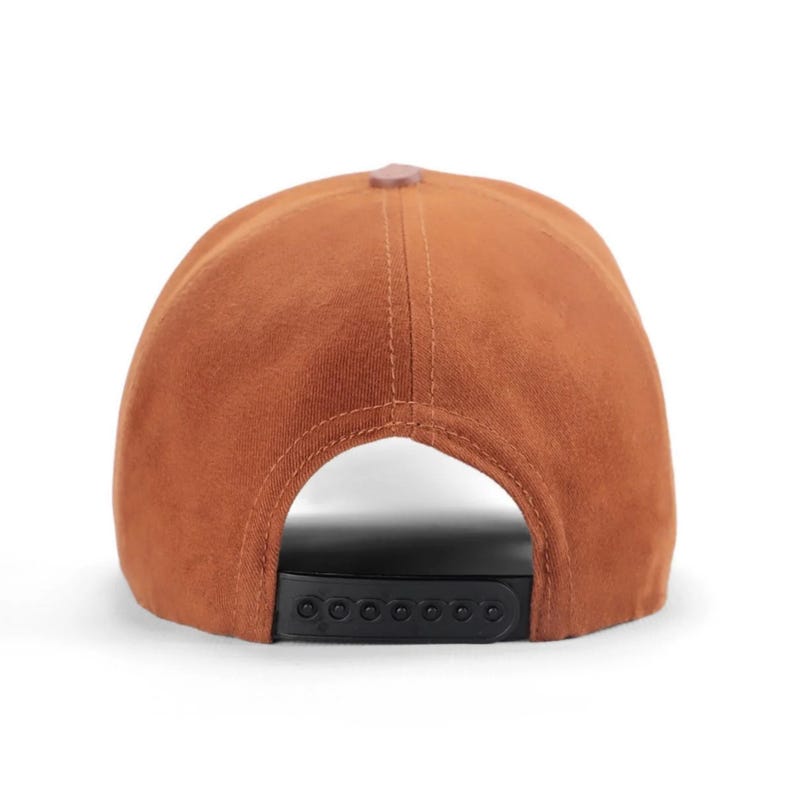 May include: A solid rust-colored baseball cap featuring a structured crown with visible vertical stitching. The back of the cap includes an adjustable black plastic snapback closure with multiple circular pegs for sizing, showing the rear view.