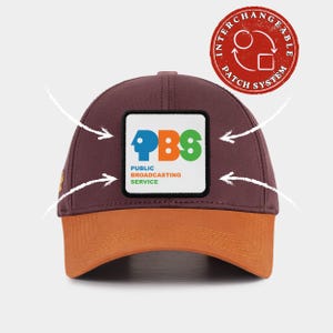 May include: A maroon baseball cap with an orange brim and a square patch on the front featuring the blue, orange, and green PBS logo and the text Public Broadcasting Service. A red circular badge in the corner reads Interchangeable Patch System.