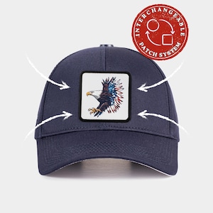 May include: A navy blue baseball cap featuring a square patch on the front panel. The patch displays a bald eagle with wings patterned in the American flag design. A red circular badge in the top right corner reads INTERCHANGEABLE PATCH SYSTEM.