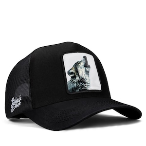 May include: A black trucker hat featuring a square patch on the front panel with a detailed illustration of a wolf howling. The side mesh panel displays the white embroidered text Black Dog. The cap has a curved brim and a structured crown design.