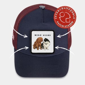 May include: Navy and burgundy trucker cap with a square patch showing two cartoon dogs and the text "MISO SUSHI". The cap has a mesh back and an interchangeable patch system.