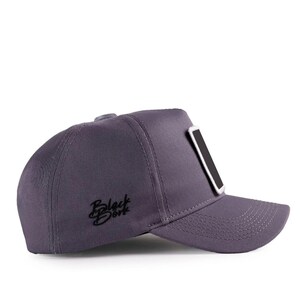 May include: A dark grey baseball cap featuring a structured crown and a curved brim. The side of the cap displays the embroidered text Black Dork in a black script font. A rectangular patch with a black centre and white border is on the front.