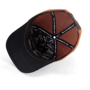 May include: A baseball cap viewed from the inside, featuring a brown crown and a black brim. The interior lining is black with white text that reads "Who are these BlackBork people?" and "BlackBork" repeated throughout the fabric panels.
