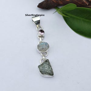 May include: A silver pendant featuring a small round faceted pink stone at the top, a smooth oval moonstone in the centre, and a rough, irregular green gemstone at the bottom, all linked together with silver settings and a bail. Text reads SilverRingEmpire.