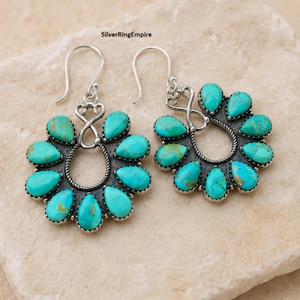 May include: A pair of silver drop earrings featuring a circular arrangement of teardrop-shaped turquoise stones. Each earring includes a twisted silver wire border and a decorative infinity-style hook attachment. The text SilverRingEmpire is visible.