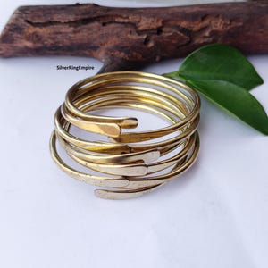Peut inclure: Un bracelet jonc en métal doré à plusieurs couches présentant un design en spirale continue avec des extrémités arrondies et aplaties. Le bracelet possède une surface polie et réfléchissante avec des variations subtiles de couleur et de texture.