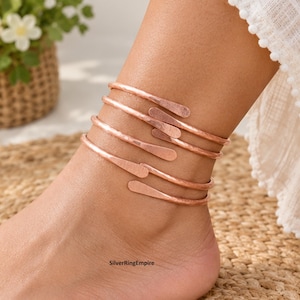 May include: A rose gold-toned metal anklet featuring a multi-wrap design with a hammered texture. The piece consists of several overlapping bands that spiral around the ankle, each ending in a flattened, rounded tip. The text SilverRingEmpire is visible.