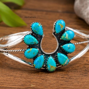 May include: A silver cuff bracelet featuring a horseshoe-shaped centrepiece adorned with seven teardrop-shaped turquoise stones. The band includes a twisted wire detail on each side, and the metal has a polished finish with dark oxidation.