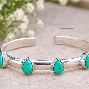 May include: A silver cuff bracelet featuring four teardrop-shaped turquoise stones set along the band. The metal has a polished finish, and the text SilverRingEmpire is visible on the upper right side of the open-ended cuff design.