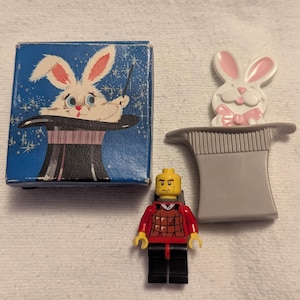 May include: A blue box with a cartoon rabbit popping out of a black top hat. A gray top hat with a white rabbit and pink bow tie. A Lego figure in a red and black outfit.