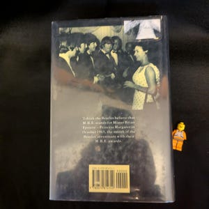 Puede incluir: Portada de libro con una foto en blanco y negro de The Beatles y una mujer. El texto dice: "Creo que los Beatles creen que M.B.E. significa Mister Brian Epstein - Princesa Margarita en octubre de 1965, el mes de la investidura de los Beatles con sus premios M.B.E."